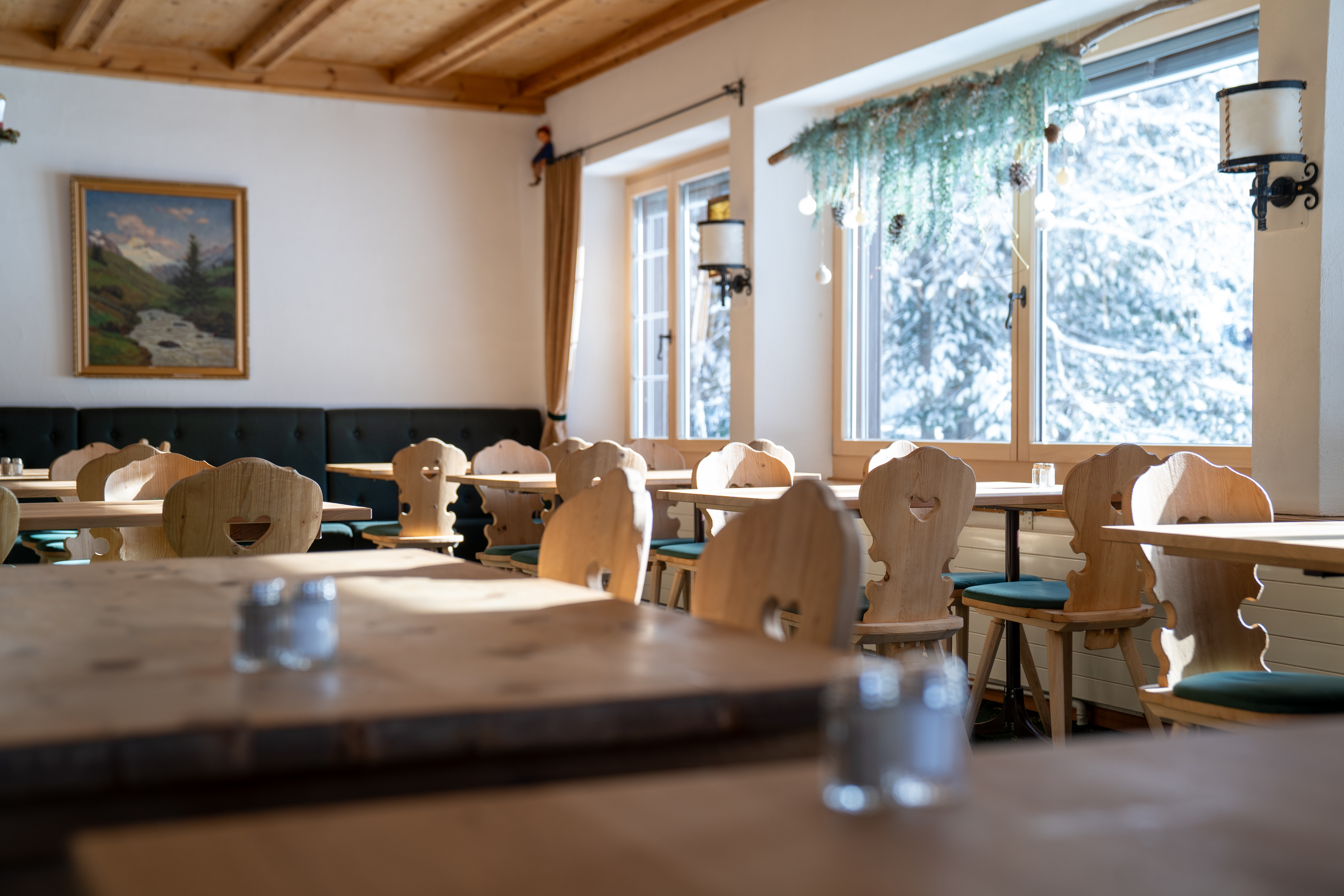 Cosy dining room at Sonne Fex featuring traditional Engadin wooden chairs, rustic timber tables and a view through snow-covered trees